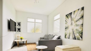 Una sala de estar moderna con un sofá gris, un reposapiés blanco, una mesa de centro redonda y un cuadro abstracto grande en la pared.