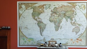 Une grande carte du monde est accrochée au mur, et devant elle se trouve une petite table sur laquelle sont posés un globe terrestre, un livre et quelques objets décoratifs.