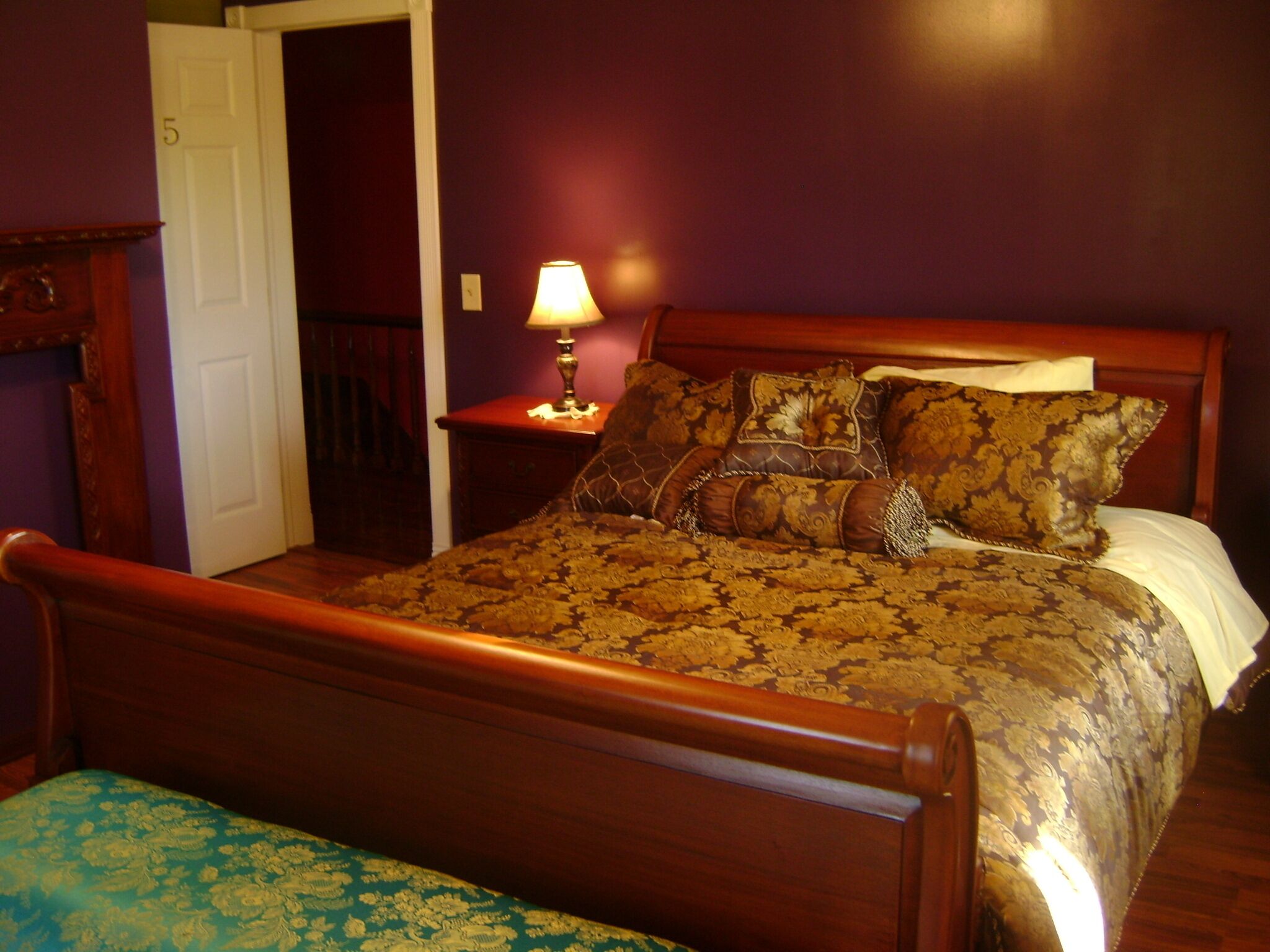A bedroom with a wooden bed, a nightstand with a lamp, and a door leading to another room.