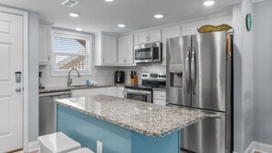 Une cuisine moderne avec des armoires blanches, des appareils en acier inoxydable, un comptoir en granit et un mur d’accent bleu.