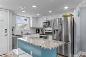 Una cocina moderna con armarios blancos, electrodomésticos de acero inoxidable, encimera de granito y una pared de acento azul.