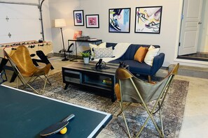 Ein Wohnzimmer mit Kicker, einer Couch, einem Couchtisch und einem Tischtennisschrank.
