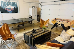Ein Zimmer mit einem Tischtennis-Tisch, einem Kicker, einer Couch, einem Couchtisch und einem Poster an der Wand.