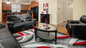 A modern living room with leather sofas, a glass coffee table, and a kitchen in the background. - Modern Updated Home, Game Room, Open Layout, Family Friendly, Near Intel & Nike 5 Min Walk to MAX (Beaverton)