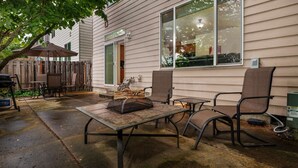 An outdoor patio with a table and chairs, a wooden deck, and a house in the background. - Modern Updated Home, Game Room, Open Layout, Family Friendly, Near Intel & Nike 5 Min Walk to MAX (Beaverton)