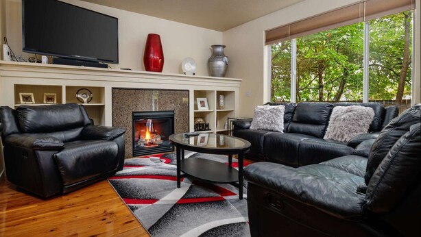 A living room with a fireplace, leather sofas, a coffee table, and a TV. - Modern Updated Home, Game Room, Open Layout, Family Friendly, Near Intel & Nike 5 Min Walk to MAX (Beaverton)