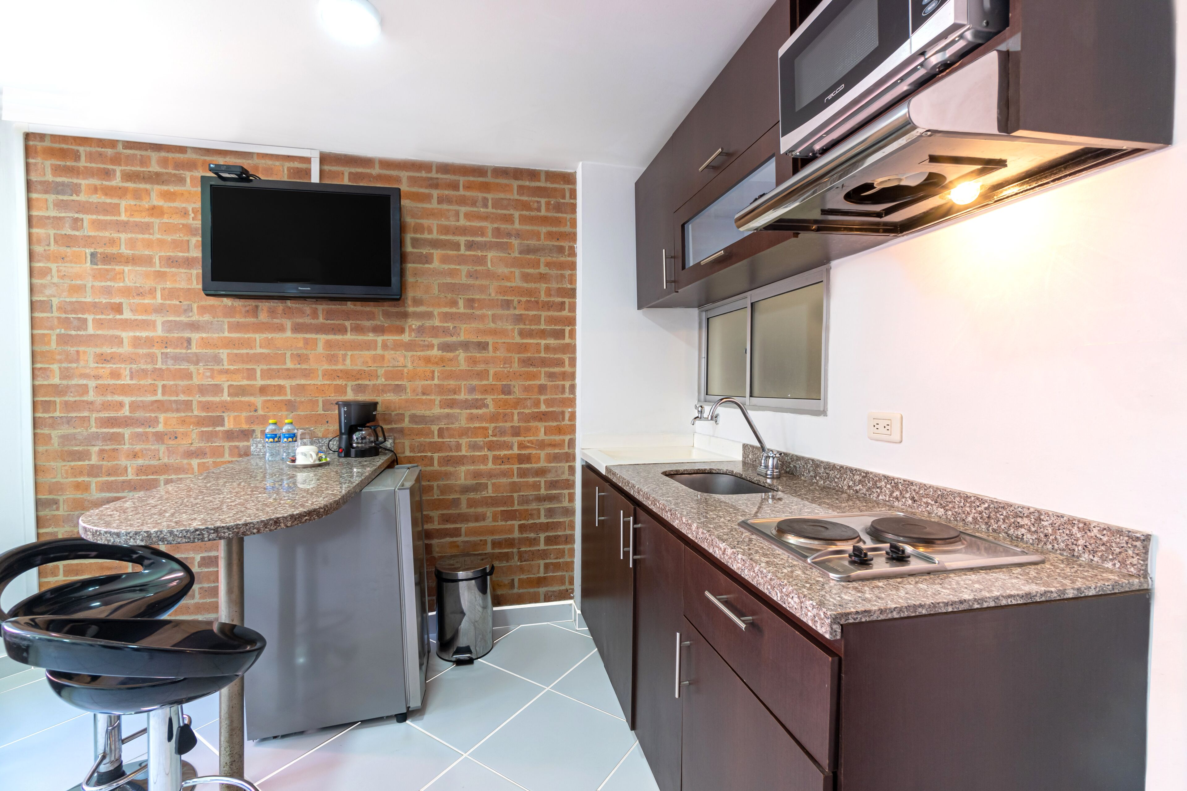 A kitchen with a brick wall, a flat-screen TV, a microwave, a stove, and a sink.