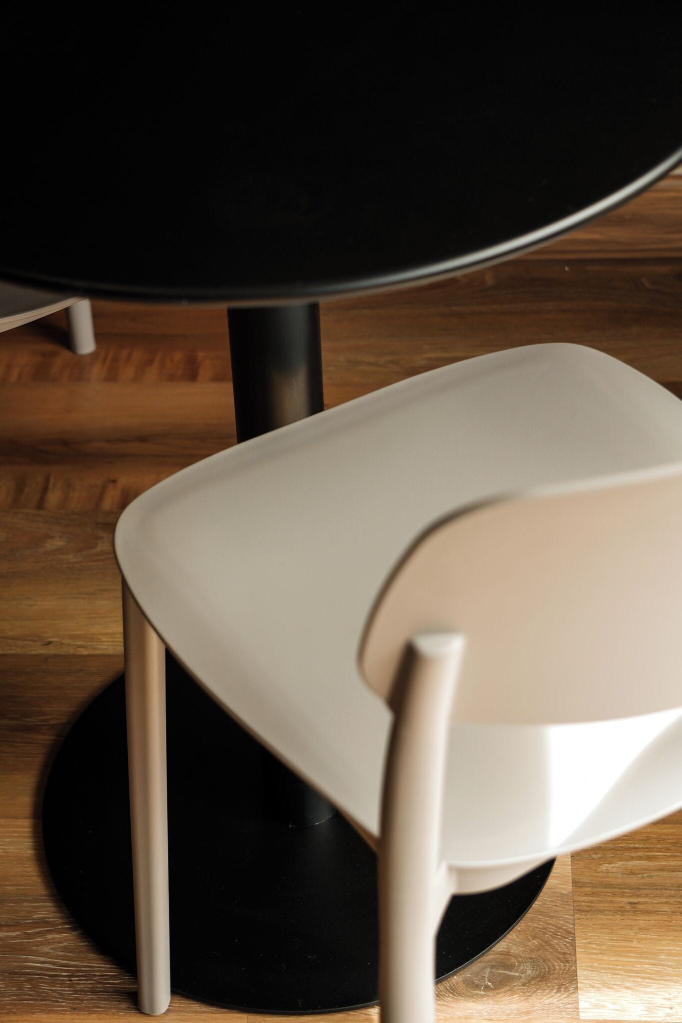 Una silla con asiento y respaldo blancos, ubicada debajo de una mesa redonda de base negra.