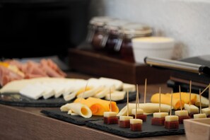A charcuterie board with various cheeses and meats, arranged on a slate board.