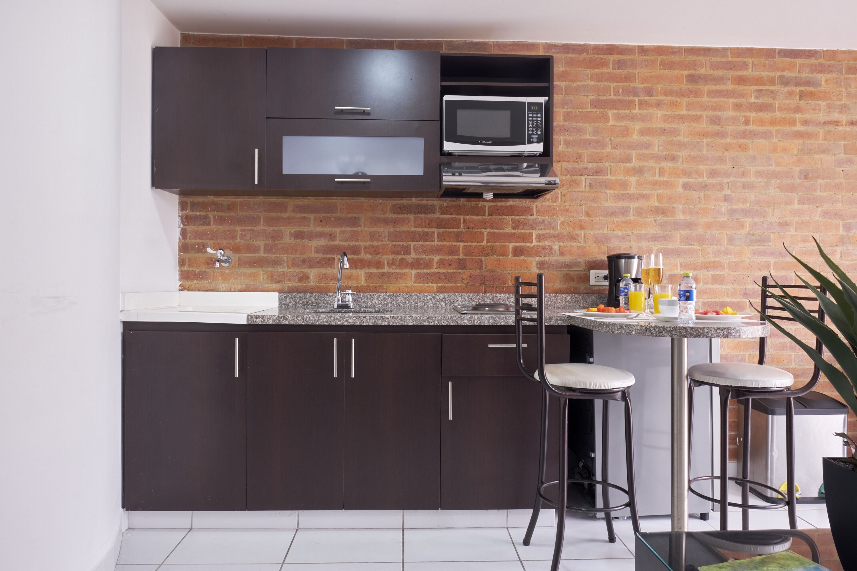 Uma cozinha moderna com armários escuros, micro-ondas, pia e um espaço bar com banquetas.