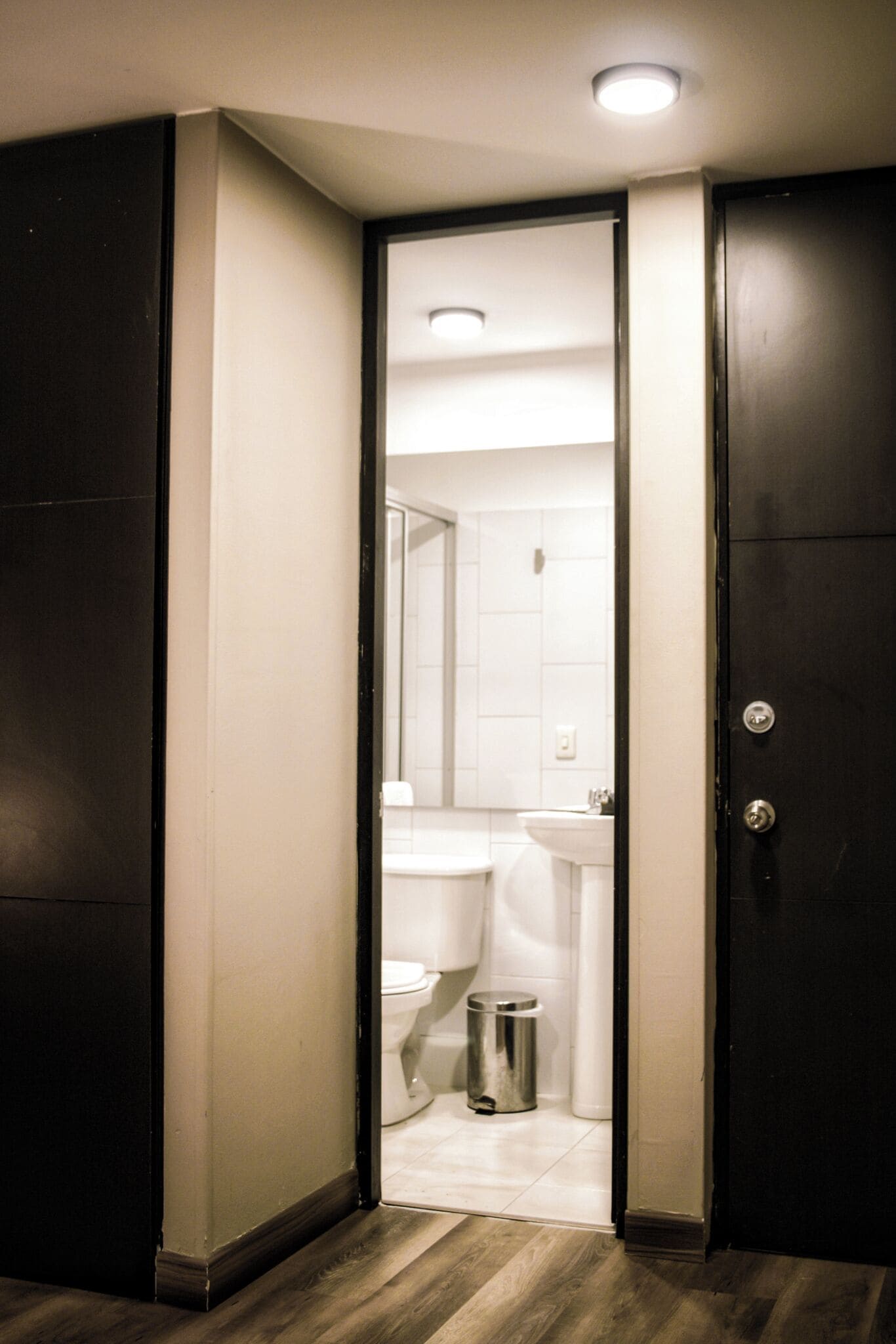 A narrow hallway leading to a bathroom with a toilet, sink, and trash can.