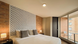 A hotel room with a large bed, a patterned wall, a balcony with a view of buildings, and a door. - Hemma Bogotá Chapinero Premium Suites Hotel (Bogotá)