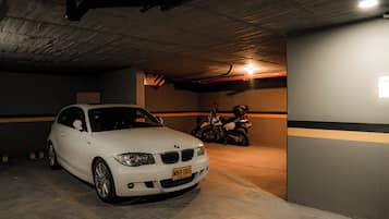 A white car parked in a dimly lit parking garage with concrete walls and a motorcycle in the background.