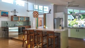 A modern kitchen with a central island, wooden chairs, and a ceiling fan.