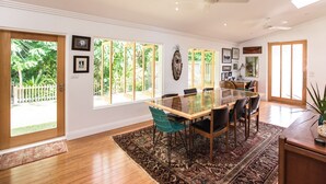 A spacious dining area with a large glass table, multiple chairs, and a view of a lush garden through large windows.