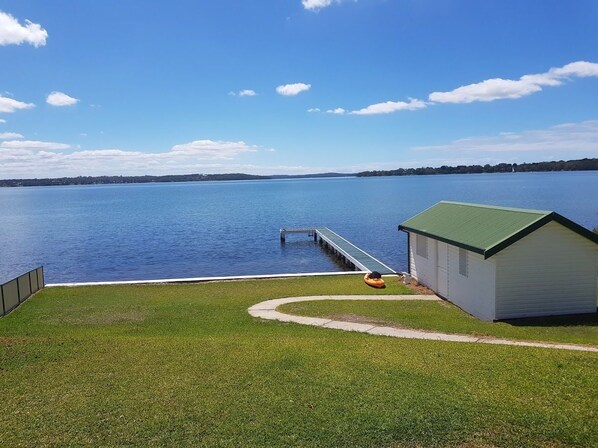 A grassy area with a dock extending into a large body of water, a small shed, and a clear sky.