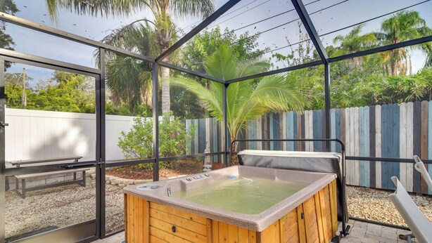 Un jacuzzi con revestimiento de madera y estructura de marco metálico, rodeado por una valla de madera y palmeras.