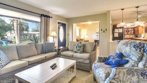 Sala de estar con un sofá, un sillón y una mesa de centro. Hay una puerta que conduce a una cocina.