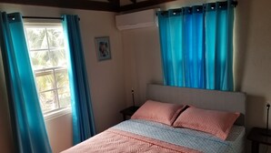 Un dormitorio con una cama, dos mesitas de noche, una ventana con cortinas y un equipo de aire acondicionado.