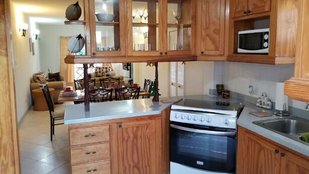 Una cocina con armarios de madera, un microondas, una estufa y un comedor con mesa y sillas.