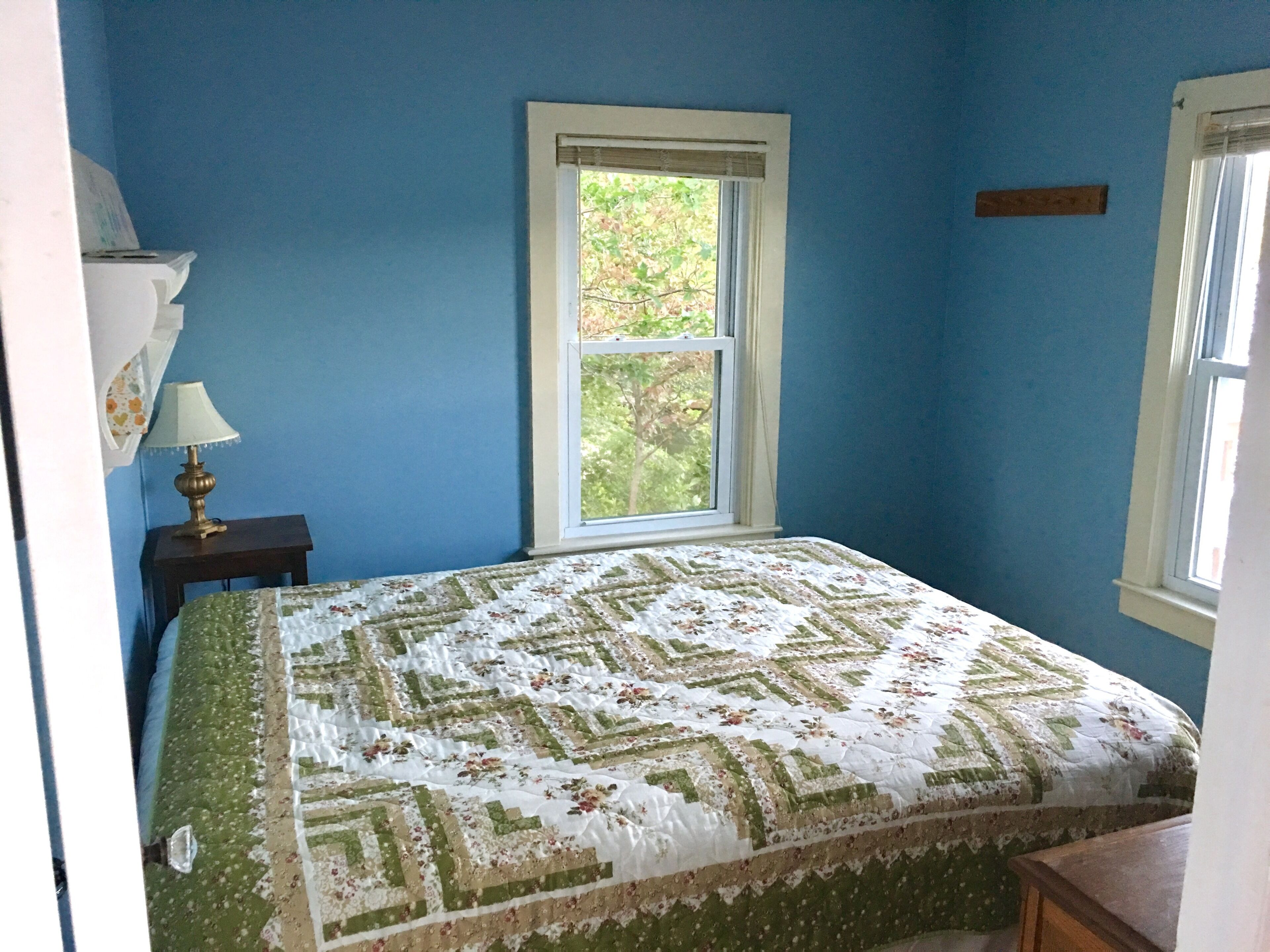 A bedroom with a bed, a window, and a nightstand with a lamp.