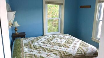 A bedroom with a bed, a window, and a nightstand with a lamp.