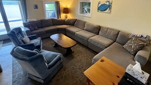 A living room with a sectional sofa, two armchairs, a coffee table, and a ceiling fan. There are windows with curtains, a lamp, and a painting on the wall. - Lakeside cottage overhanging the water, beautiful window views across the lake (Ledyard)