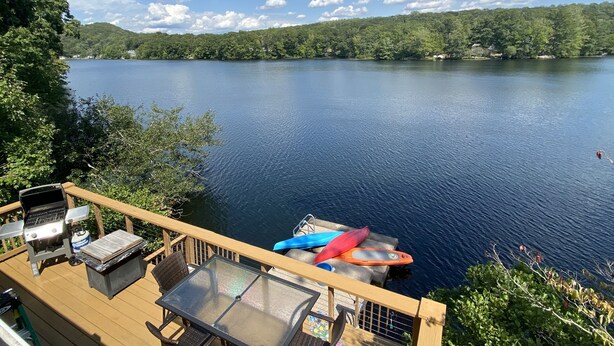 A deck with a grill, a glass table, and kayaks by a lake. - Lakeside cottage overhanging the water, beautiful window views across the lake (Ledyard)