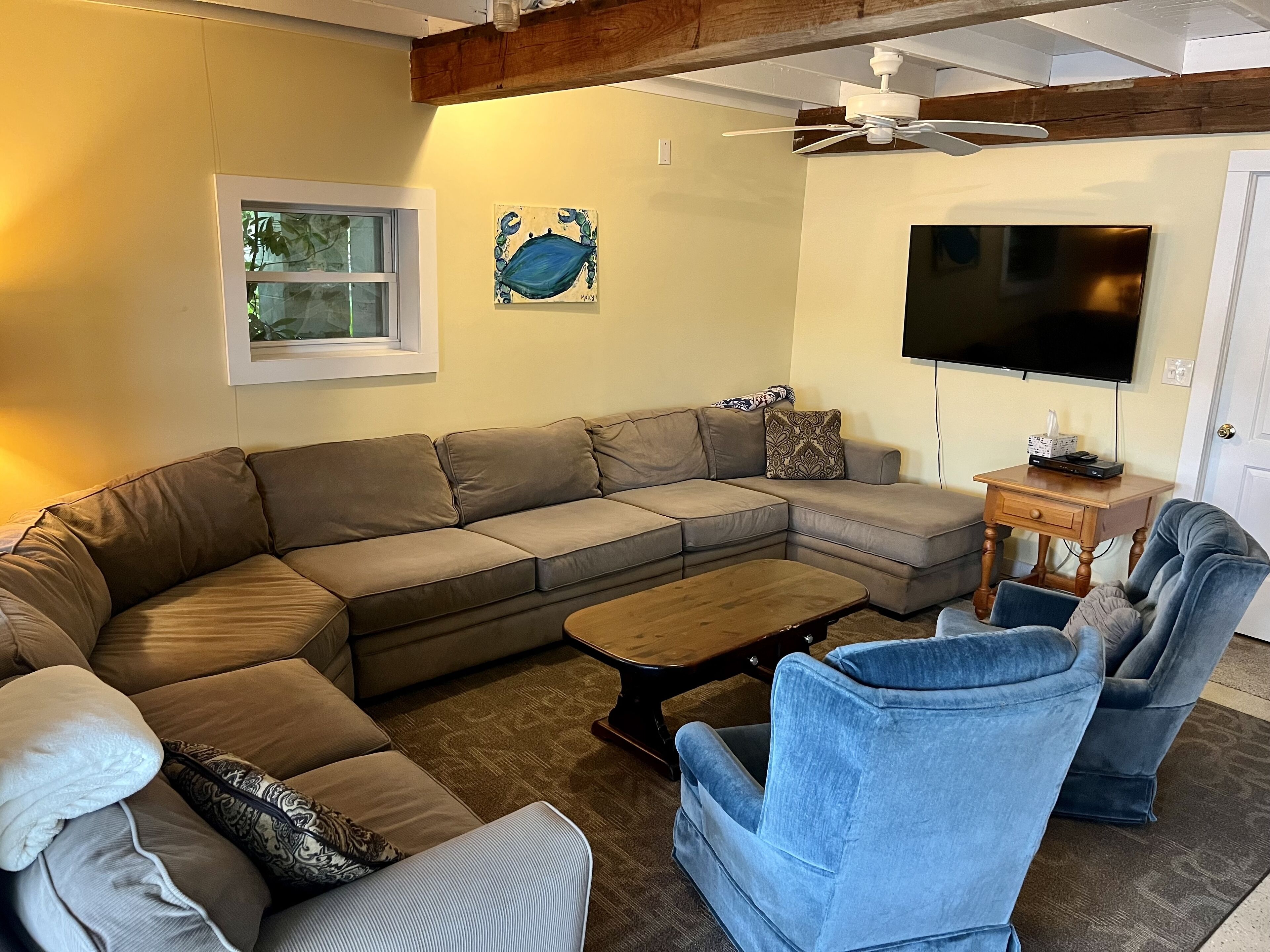 A living room with a sectional sofa, a coffee table, two armchairs, a TV, and a ceiling fan.