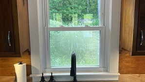 A kitchen with a window, a sink, a paper towel holder, and a soap dispenser. - Lakeside cottage overhanging the water, beautiful window views across the lake (Ledyard)