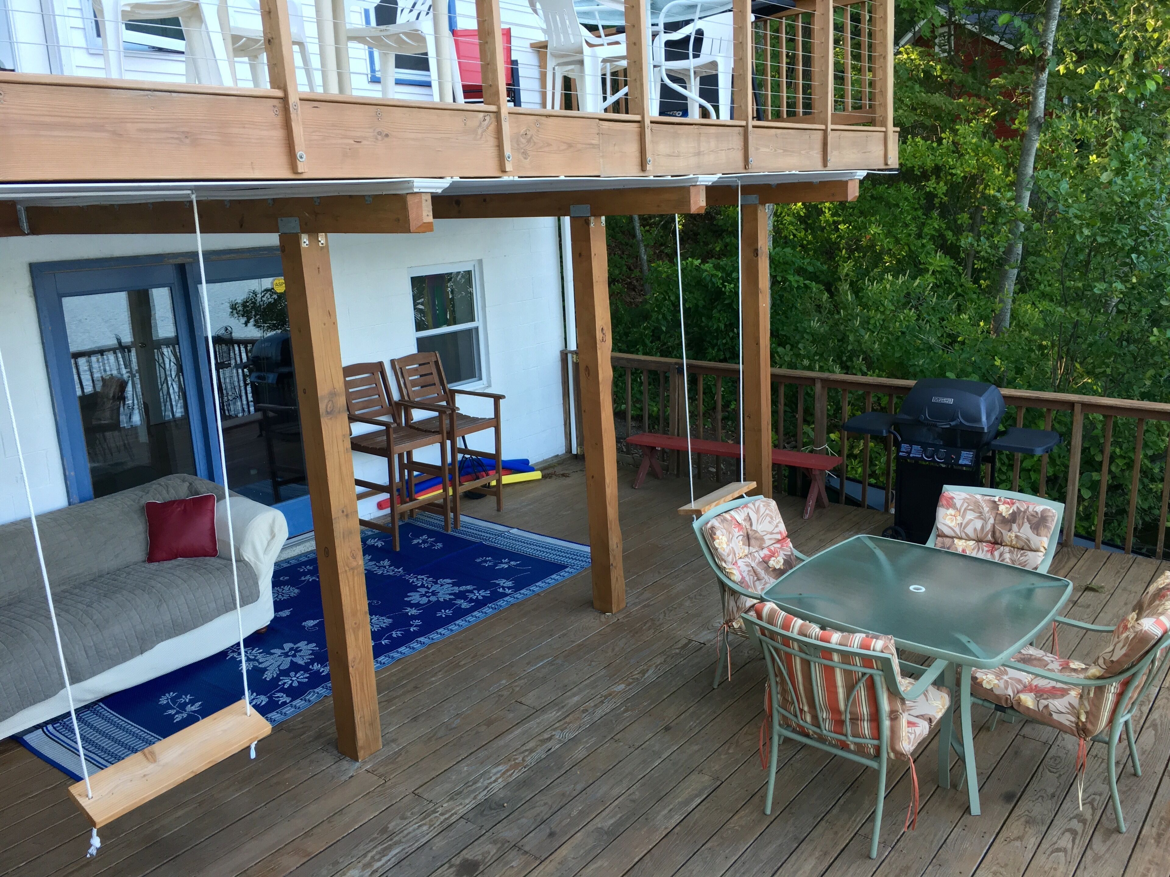 Une terrasse en bois avec une balançoire, une table en verre et des chaises.