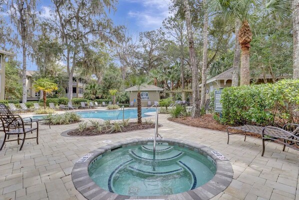 A swimming pool with a hot tub, surrounded by lounge chairs and palm trees.