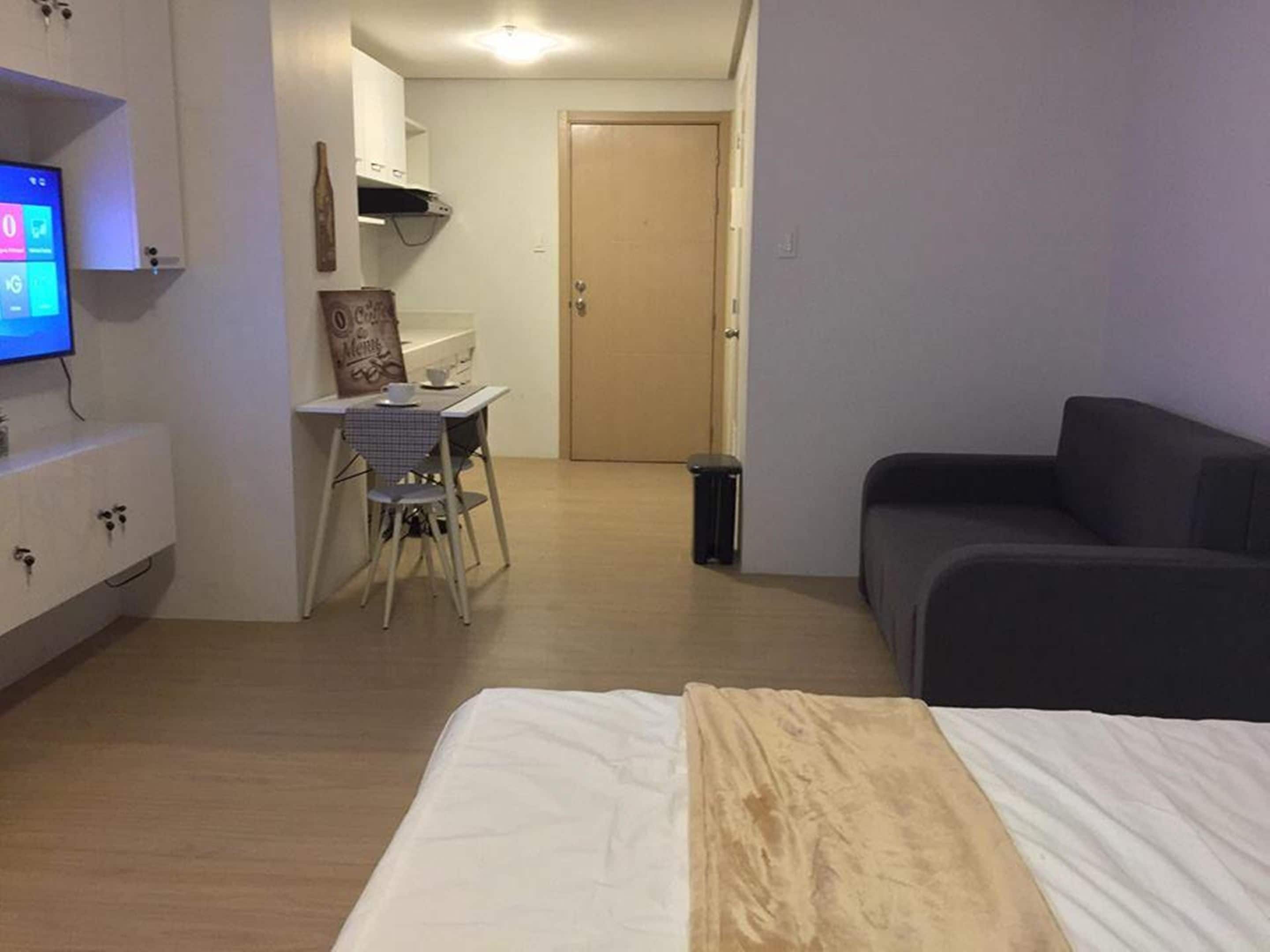 Une chambre d’hôtel de taille modeste, comprenant un lit, un petit bureau avec une chaise, un téléviseur et une porte donnant sur une autre pièce.