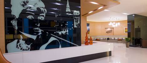 A modern lobby with a reception desk, a large abstract wall art, and a seating area with sofas and a coffee table.