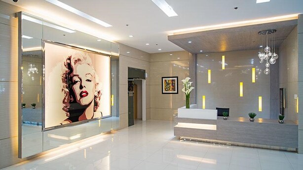 A modern lobby with a large poster, a reception desk, and a chandelier. - M Place at Abs by Noemi (Quezon City)