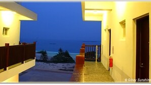 A corridor leading to a balcony overlooking a beach at dusk.