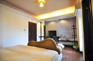 Habitación de hotel con cama, televisión, una mesita y ventana con persianas.