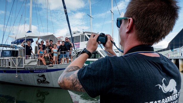 Uma pessoa fotografando um grupo em um barco chamado 'Coral Sea Dreaming'.