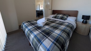 A hotel room with a bed, a nightstand, a lamp, and a view of the hallway and kitchen.
