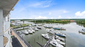 A marina with boats docked, a bridge in the background, and a building with a balcony overlooking the water. - Waterfront Condo | Marina Views | Pools & Lazy River | On-Site Dining | Sleeps 8 (Orange Beach)