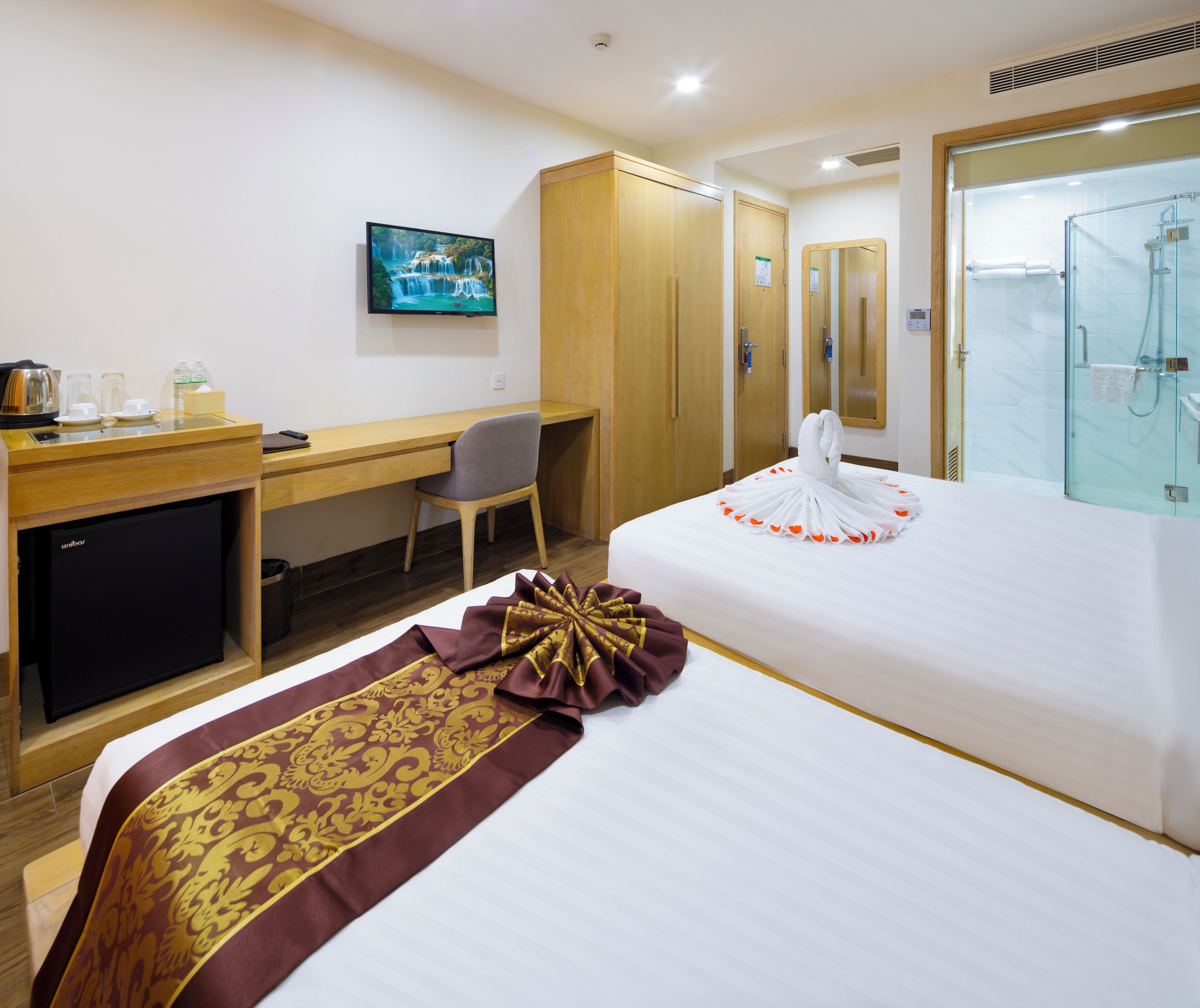 A hotel room with a bed, a desk, a chair, a television, and a shower area.