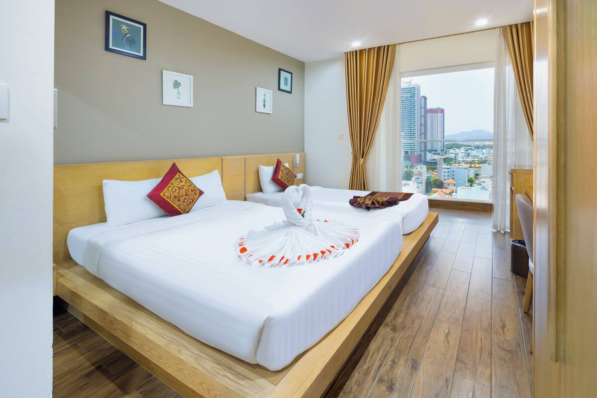 Une chambre d’hôtel avec un grand lit, une tête de lit en bois et une vue sur la ville par la fenêtre.
