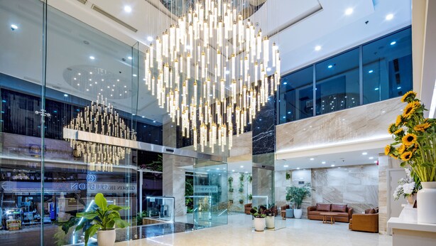 A spacious lobby with a high ceiling, modern chandeliers, and a seating area with sofas and potted plants.