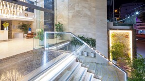 A modern hotel lobby with a marble staircase, glass railings, and indoor plants.
