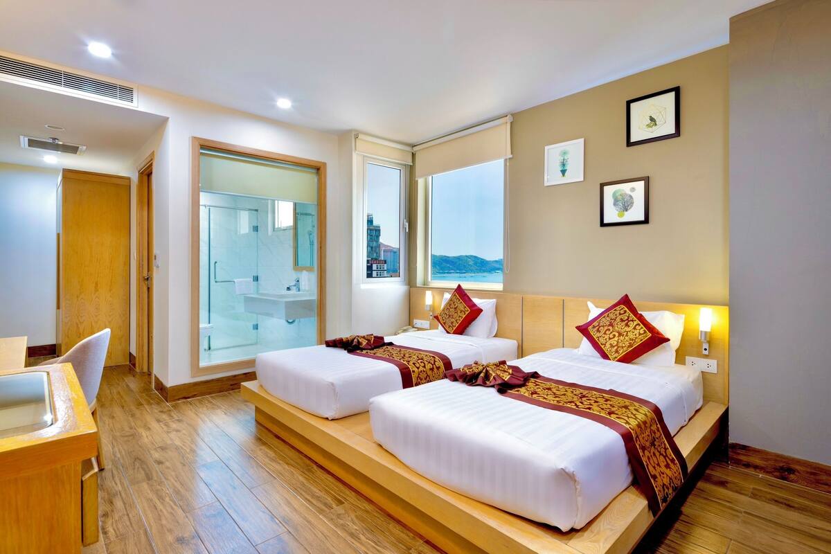 Une chambre d’hôtel avec deux lits, un bureau et une salle de bain visible à travers une porte en verre.