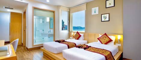 A hotel room with two beds, a desk, and a bathroom visible through a glass door.