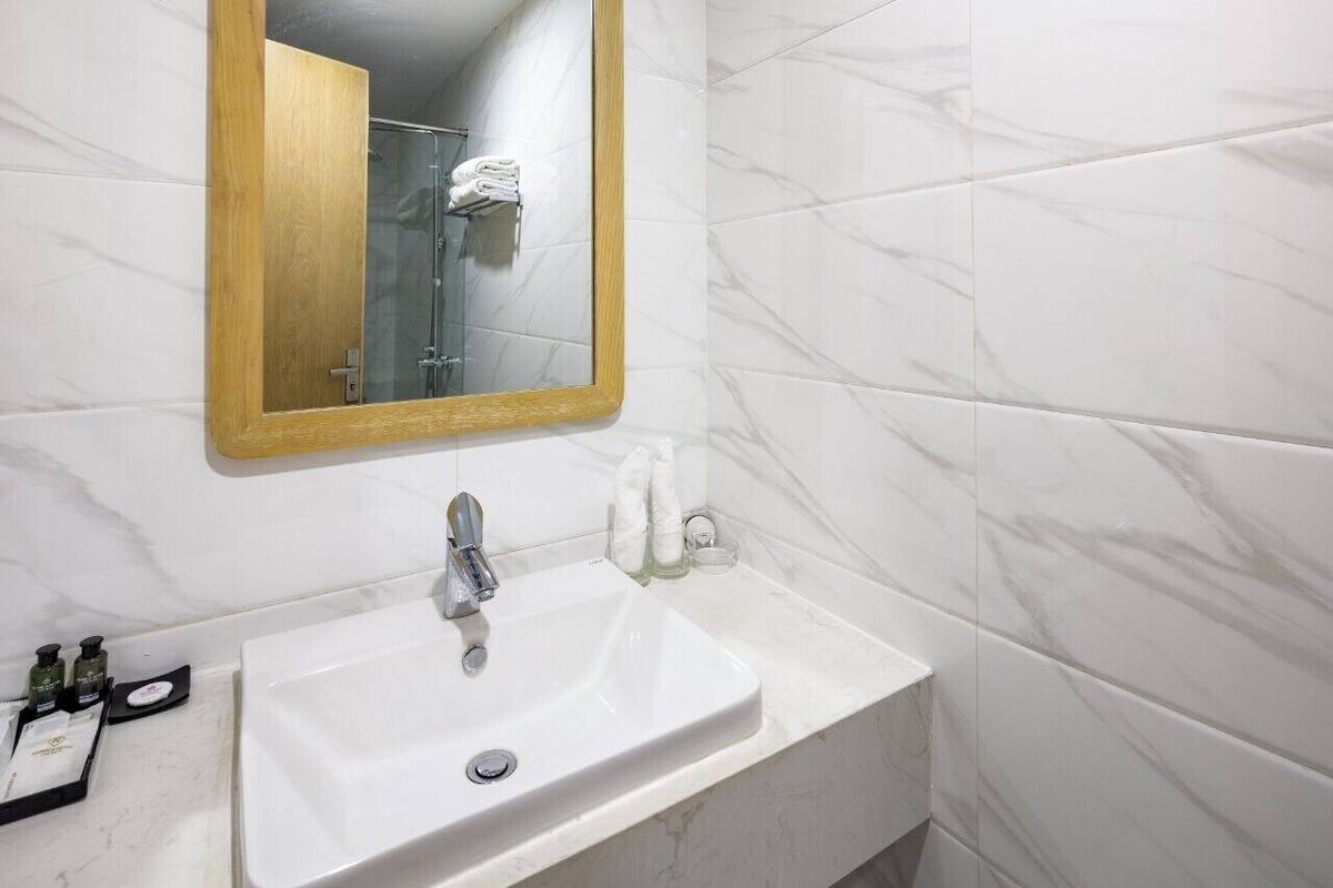 Une salle de bain avec un lavabo blanc, un miroir encadré en bois et des murs à motifs de marbre.