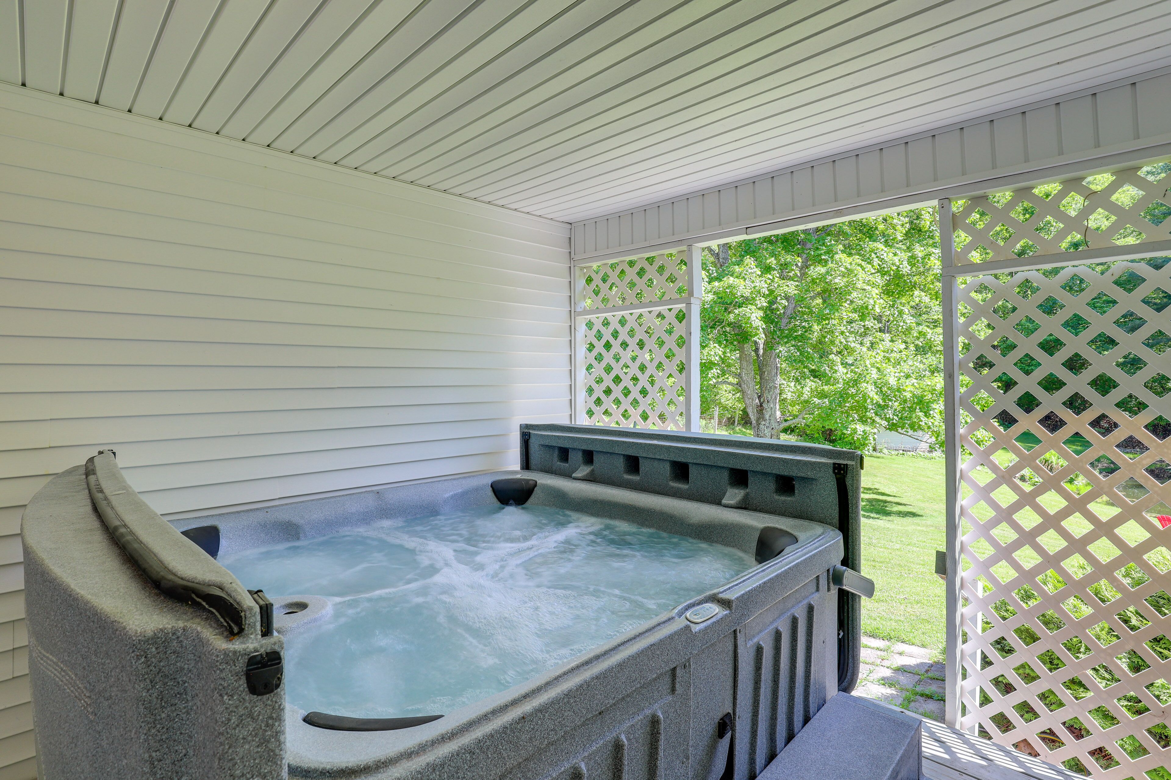 A hot tub in a covered outdoor area with a view of a green lawn and trees.
