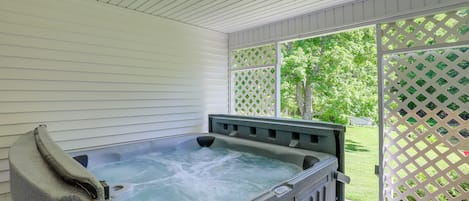 A hot tub in a covered outdoor area with a view of a green lawn and trees.