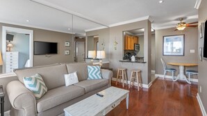 A modern living room with a sofa, coffee table, and a dining area with stools and a table. - Refined Coastal Studio | Near the Gulf (Destin)